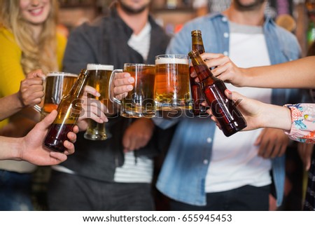 Close up of friends toasting beer glasses and bottles in pub