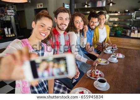 Smiling friends taking photo through mobile phone in pub