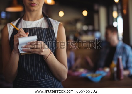 Mid section of waitress taking order at restaurant