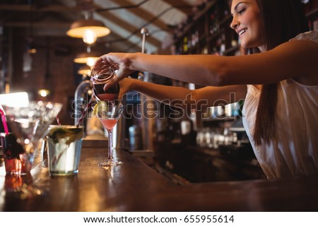 Pretty bartender pouring a cocktail drink in the glass at bar