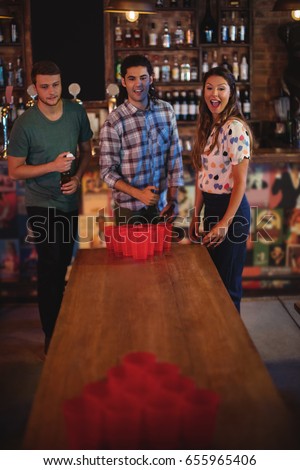 Group of happy friends playing beer pong game in pub