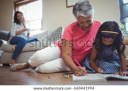Grandmother and granddaughter coloring book in living room at home