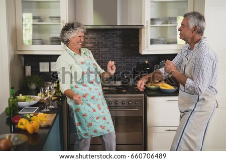 Active senior couple dancing in kitchen at home