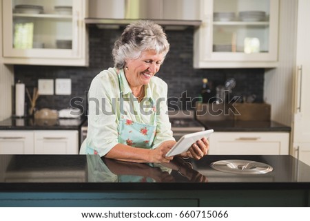 Smiling senior woman using digital tablet on counter in kitchen at home