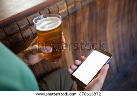 Cropped hands of man using phone while having beer at bar counter