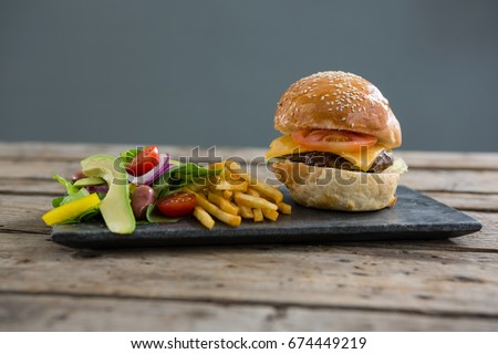 Salad with french fries and burger on slate at table against wall