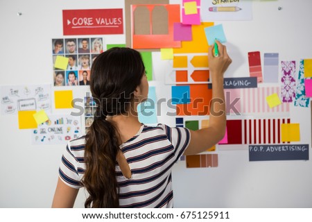 Rear view of businesswoman writing on sticky note in creative office