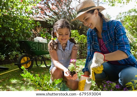 Smiling mother teaching daughter to plant seedlings while gardening in backyard