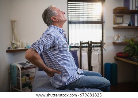 Side view of senior male patient suffering from back ache while looking up on bed at hospital ward