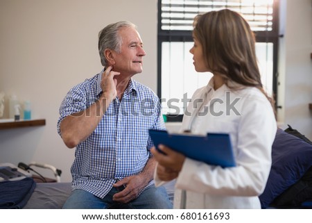 Senior male patient showing neck sprain to female doctor with file at hospital ward