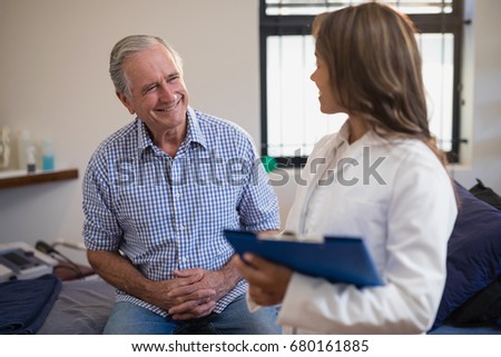 Smiling senior male patient looking at female therapist with file at hospital ward
