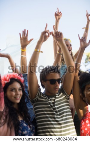 Young friends dancing with arms raised against sky during music festival
