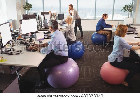 Business people sitting on exercise balls while working at desk in office