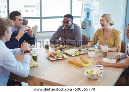 Happy business colleagues having lunch on table at office cafeteria