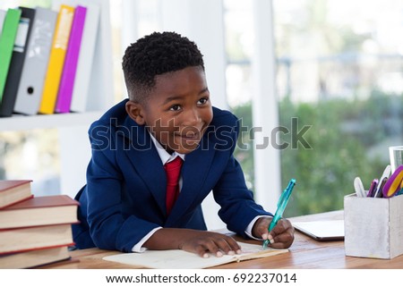 Smiling businessman looking away while writing on book at desk in office