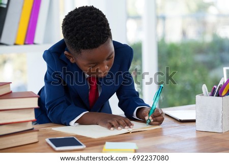 Boy imitating as businessman writing on diary at desk in office