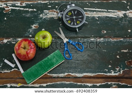 Close-up of apple, alarm clock, duster, scissors and chalk on wooden table