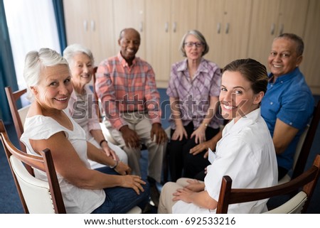Portrait of smiling female doctor and seniors sitting on chairs at retirement home