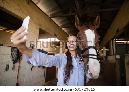 Smiling female vet taking selfie with horse in stable