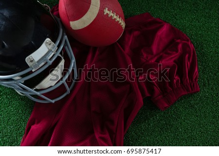 Close-up of American football jersey, head gear and football lying on artificial turf