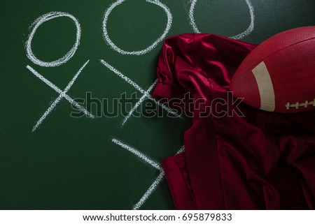 Close-up of American football jersey and football lying on green board with strategy drawn on it