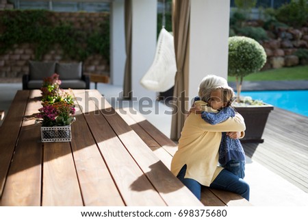 Granddaughter and grandmother embracing in a deck shade on a sunny day
