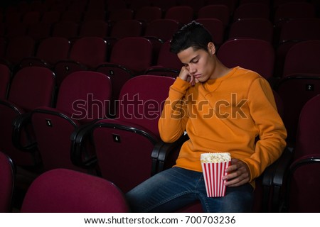 Bored man with popcorn sleeping in theatre