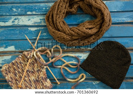High angle view of muffler with knit hat and knitting needles on wooden table