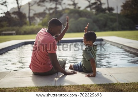 Smiling father and son giving high five to each other near poolside