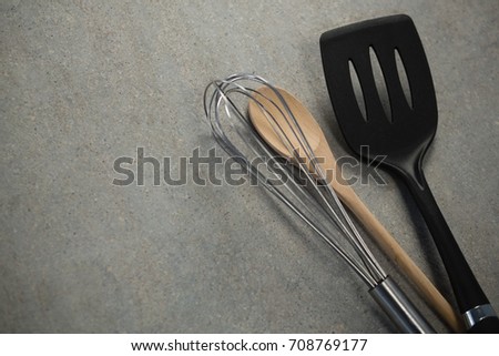 High angle view of wire whisk and wooden spoon by spatula at table