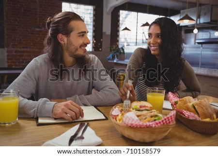 Smiling young friends having food at table in cafe