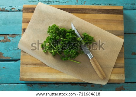 Overhead view of coriander leaves, wax paper and knife on chopping board