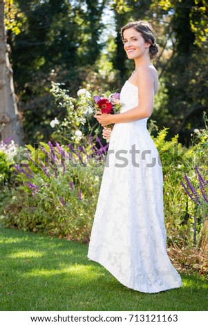 Smiling bride holding bouquet while standing on grassy field at yard