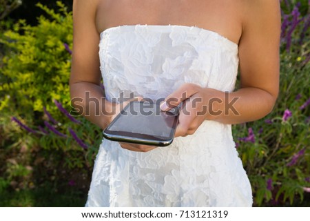 Midsection on bride using smart phone while standing against plants in yard
