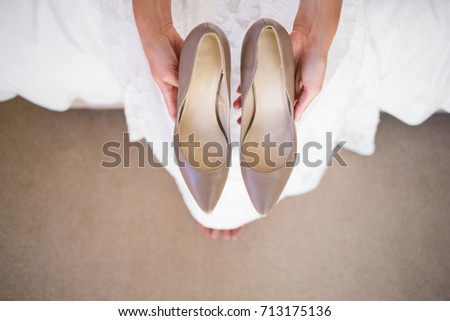 High angle low section of bride holding shoes while sitting in fitting room