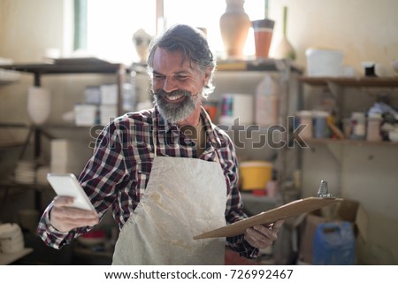 Happy potter using mobile phone in pottery workshop