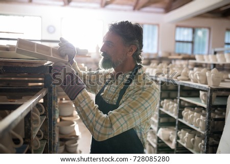 Male potter placing craft product on shelf in pottery workshop