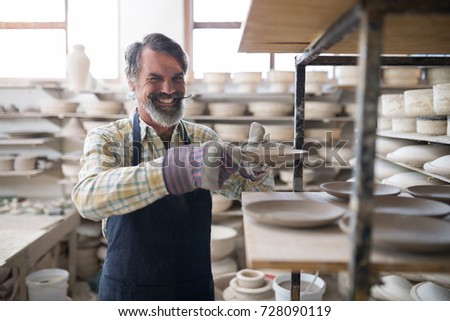 Happy male potter placing plate ob shelf in pottery workshop