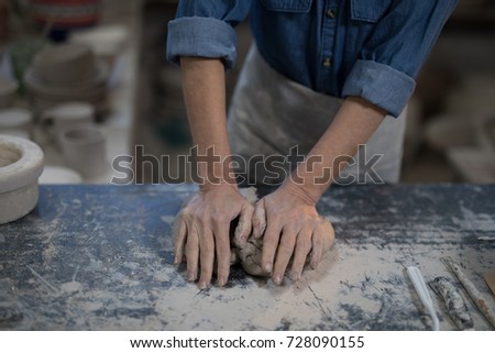 Mid section of female potter molding a clay in pottery shop