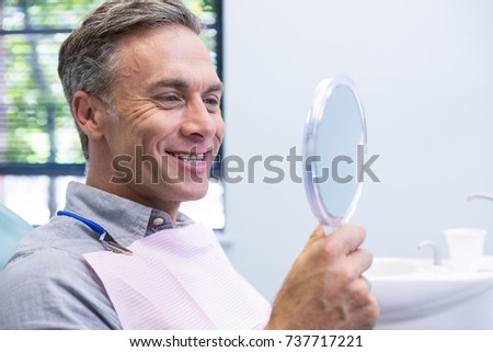 Portrait of smiling man looking in mirror at dental clinic