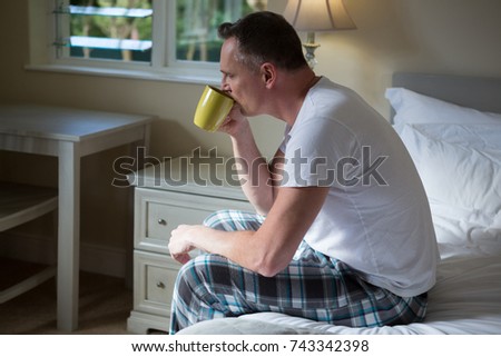 Man drinking cup of coffee in bedroom at home