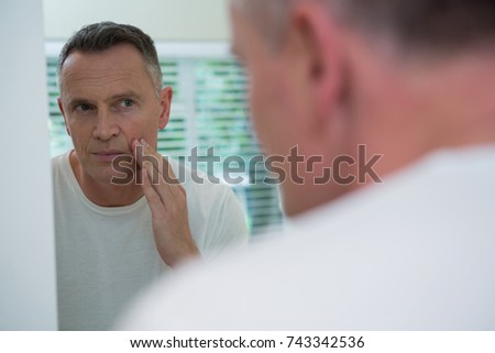 Man looking his face in the mirror after shaving standing in the bathroom
