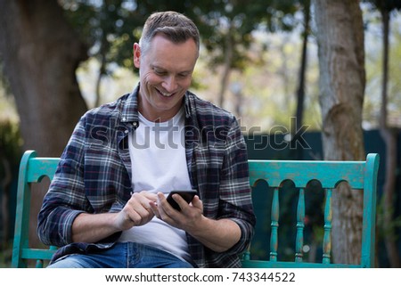 Smiling man using mobile phone on bench in garden