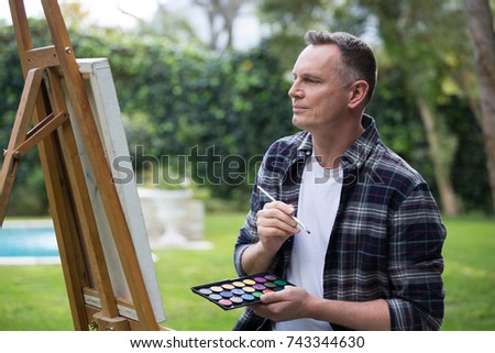Smiling man painting on canvas in garden