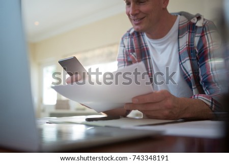 Smiling man using mobile phone and looking at document