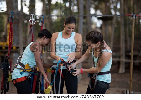 Happy female friends getting their belt tied perform zip line in park