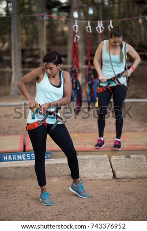 Female friends getting their belt tied to perform zip line in park
