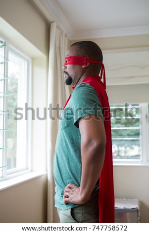 Man in superhero costume looking through window at home