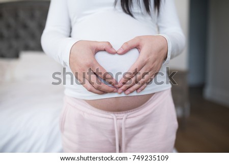 Mid section of woman forming heart shape on stomach with hands