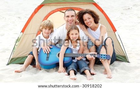 Happy family camping on beach playing a guitar